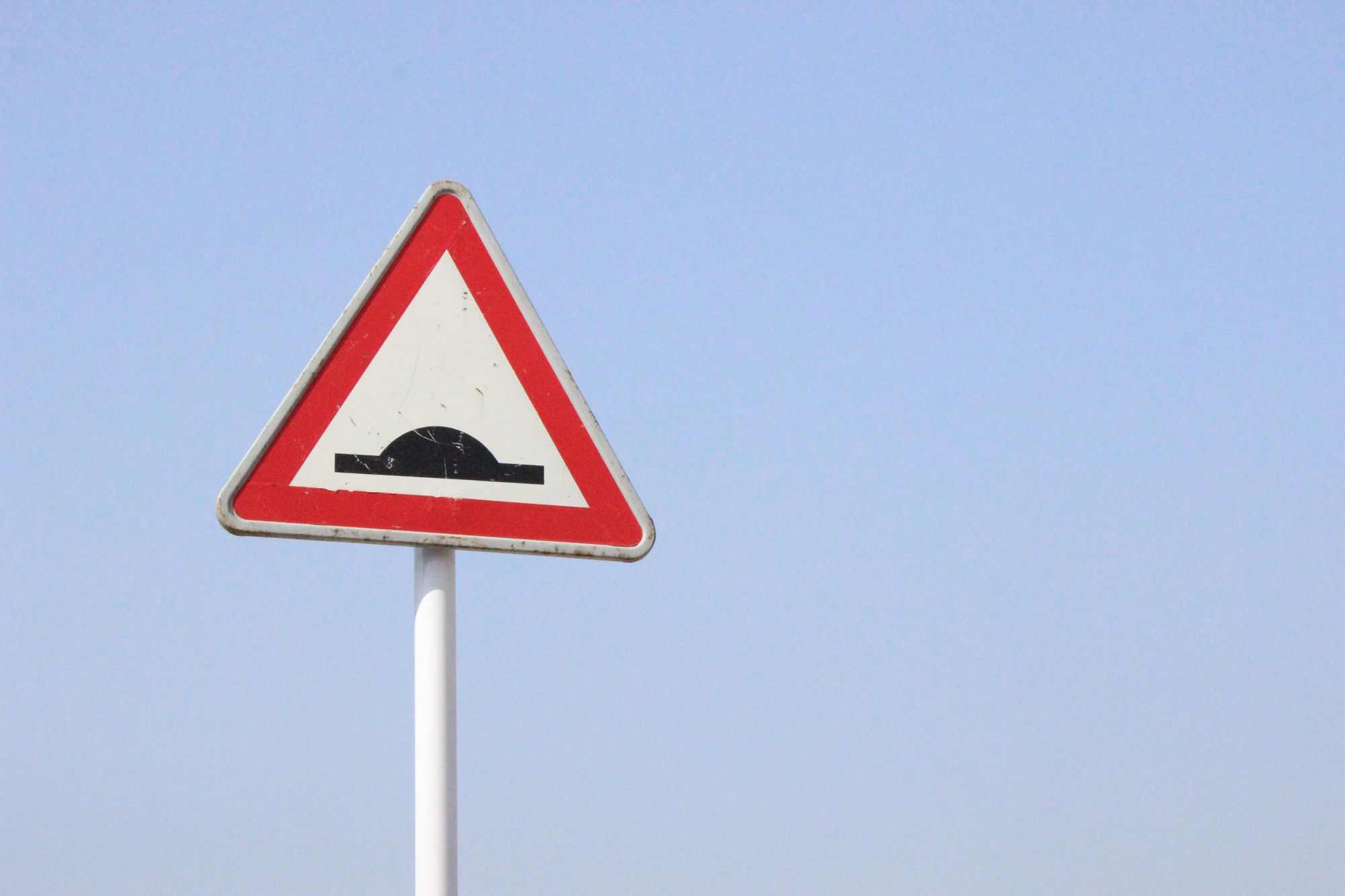 Road sign with a the symbol for a hump in the road against a blue sky.