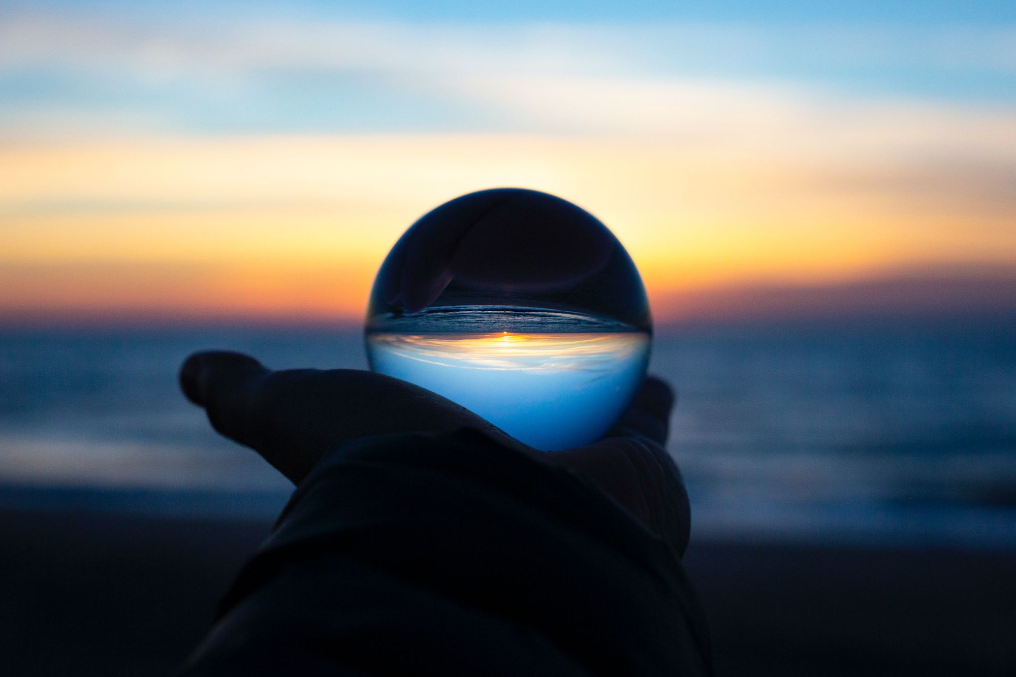 Silhouette of a hand holding a glass orb against a sunset.
